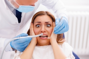 woman afraid of dentist holding her face as dentist has tools next to it