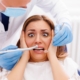 woman afraid of dentist holding her face as dentist has tools next to it