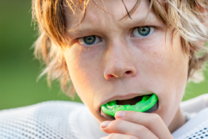 young boy playing football with a bright green mouth guard in his mouth