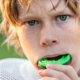 young boy playing football with a bright green mouth guard in his mouth